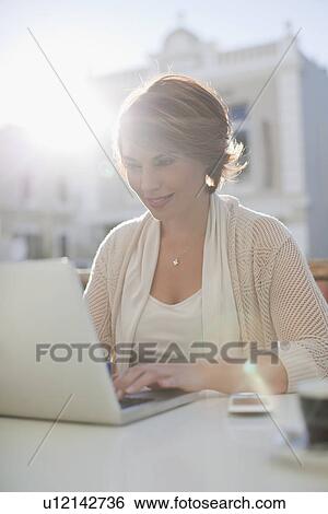 Woman using laptop at sidewalk cafe View Large Photo Image Stock Photograph - Woman using laptop at sidewalk cafe. Fotosearch