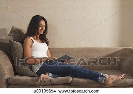 Picture - Woman using tablet computer on sofa. Fotosearch