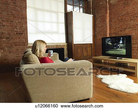 Stock Image - Woman watching television on sofa. Fotosearch