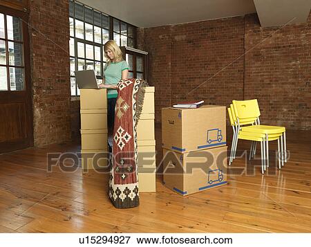 Stock Photo - Woman with cardboard boxes in new home. Fotosearch