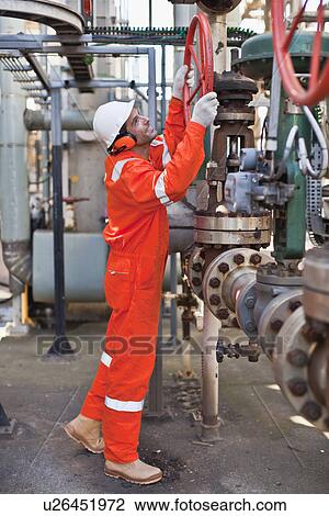 Stock Image - Worker adjusting gauge at oil refinery. Fotosearch
