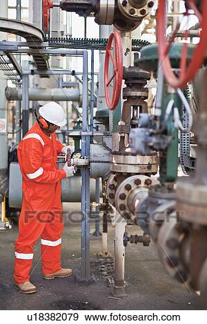 Stock Photo - Worker adjusting gauge at oil refinery. Fotosearch