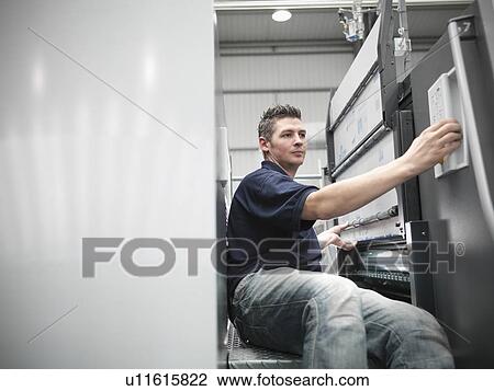 Stock Image - Worker changing plates on printing press. Fotosearch