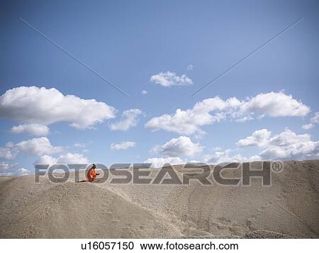 Stock Image - Worker climbing sand dunes in quarry. Fotosearch