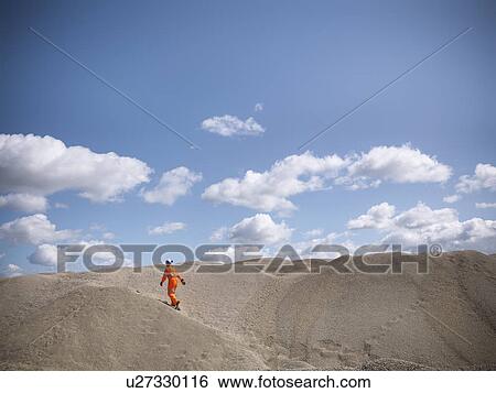 Stock Photograph - Worker climbing sand dunes in quarry. Fotosearch