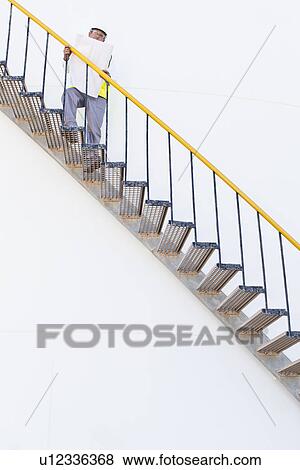 Stock Photo - Worker climbing steps at chemical plant. Fotosearch