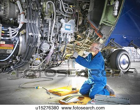 Stock Image - Worker examining airplane machinery. Fotosearch