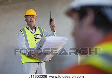Worker holding blueprints on site View Large Photo Image Stock Photograph - Worker holding blueprints on site. Fotosearch