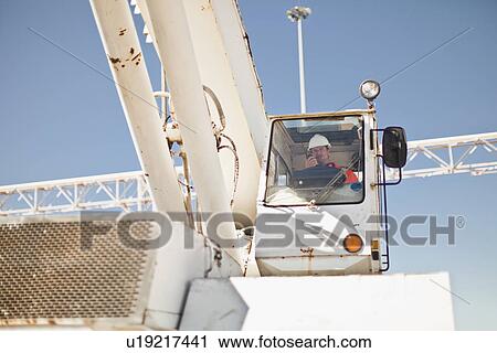 Stock Image - Worker operating crane at oil refinery. Fotosearch