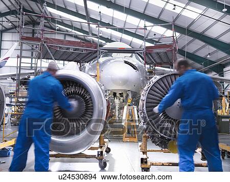 Picture - Worker pushing airplane engines on carts. Fotosearch