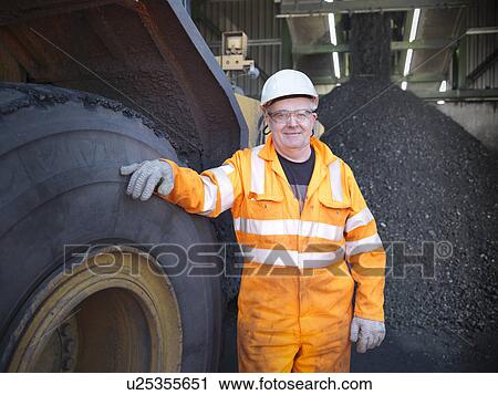 Stock Image - Worker standing by truck at coal mine. Fotosearch