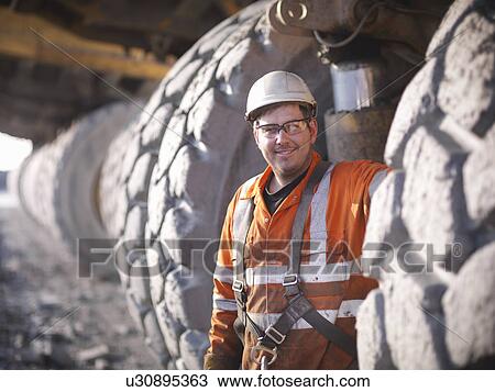 Stock Image - Worker standing by trucks in coal mine. Fotosearch