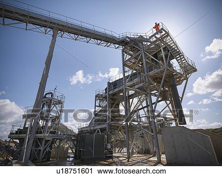 Stock Image - Worker standing on conveyor in quarry. Fotosearch