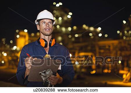 Stock Photo - Worker with clipboard at oil refinery. Fotosearch