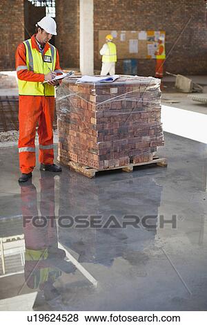 Worker writing on clipboard on site View Large Photo Image Stock Photo - Worker writing on clipboard on site. Fotosearch