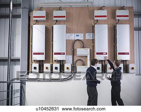 Stock Image - Workers checking solar panel controls. Fotosearch