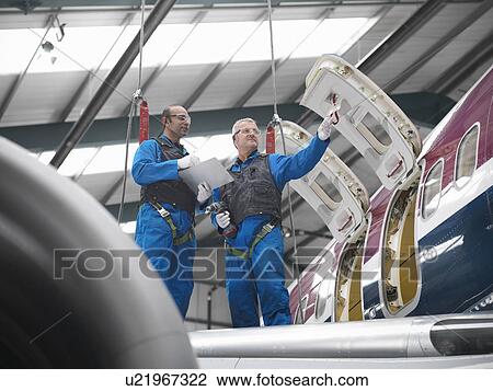 Stock Image - Workers examining airplane in hangar. Fotosearch