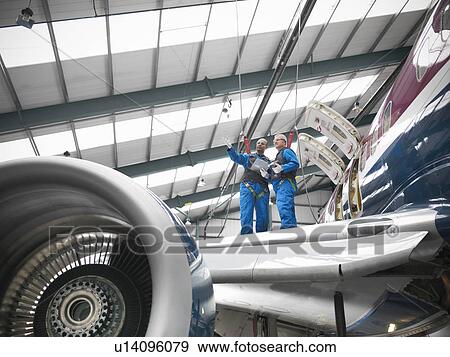 Stock Photo - Workers examining airplane in hangar. Fotosearch