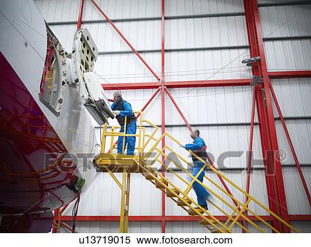 Stock Photography - Workers examining airplane in hangar. Fotosearch