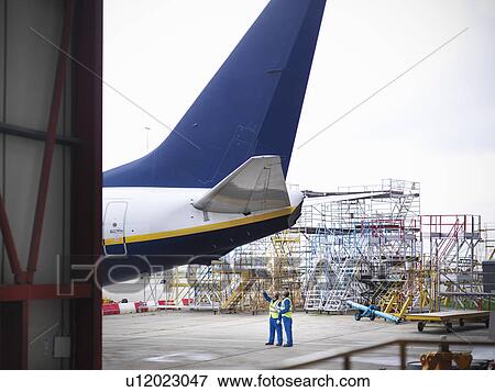 Stock Photo - Workers examining underside of airplane. Fotosearch