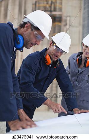 Stock Image - Workers reading blueprints at plant. Fotosearch