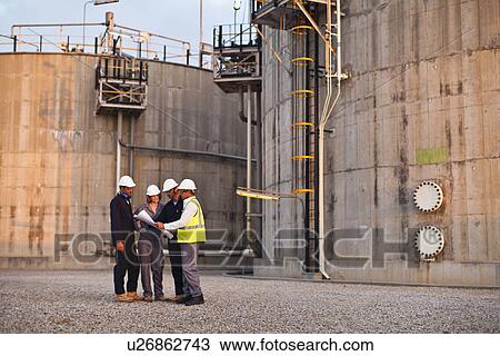 Stock Image - Workers reading blueprints at plant. Fotosearch