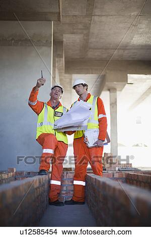 Picture - Workers reading blueprints on site. Fotosearch