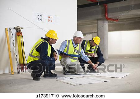 Stock Image - Workers reading blueprints on site. Fotosearch