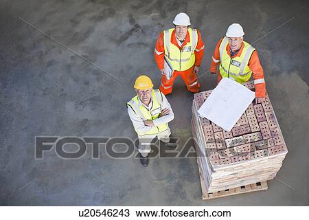 Stock Image - Workers reading blueprints on site. Fotosearch