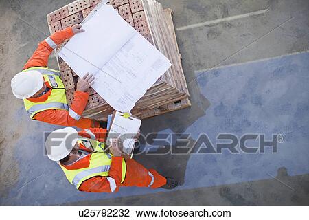 Stock Image - Workers reading blueprints on site. Fotosearch