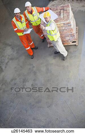 Stock Image - Workers reading blueprints on site. Fotosearch
