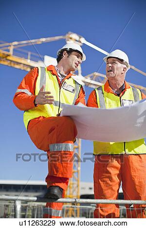 Stock Photo - Workers reading blueprints on site. Fotosearch