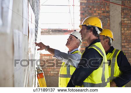 Stock Photo - Workers reading blueprints on site. Fotosearch