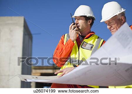 Workers reading blueprints on site View Large Photo Image Stock Photo - Workers reading blueprints on site. Fotosearch