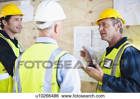 Workers reading blueprints on site View Large Photo Image Stock Photograph - Workers reading blueprints on site. Fotosearch