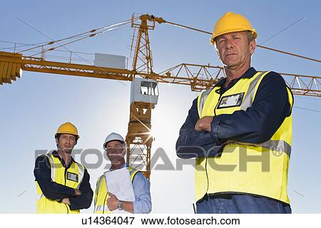 Workers standing at construction site View Large Photo Image Stock Photo - Workers standing at construction site. Fotosearch