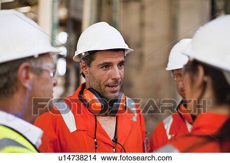 Picture - Workers talking at oil refinery. Fotosearch