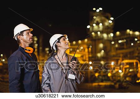 Stock Image - Workers talking at oil refinery. Fotosearch