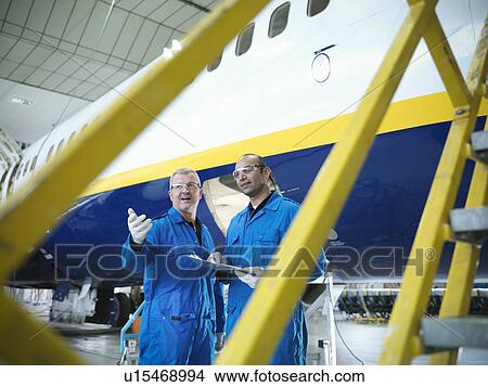 Picture - Workers talking in airplane hangar. Fotosearch