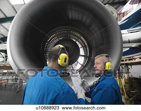Stock Image - Workers talking in airplane hangar. Fotosearch