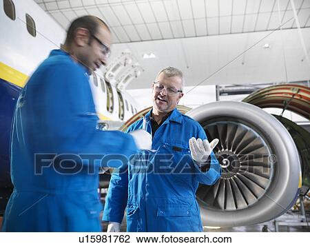 Stock Image - Workers talking in airplane hangar. Fotosearch