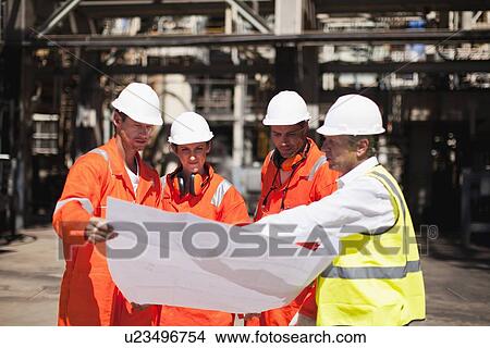 Picture - Workers with blueprints at oil refinery. Fotosearch