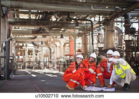 Stock Image - Workers with blueprints at oil refinery. Fotosearch