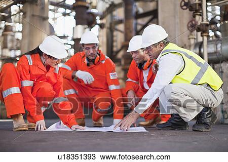 Stock Image - Workers with blueprints at oil refinery. Fotosearch