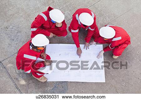 Stock Image - Workers with blueprints at oil refinery. Fotosearch