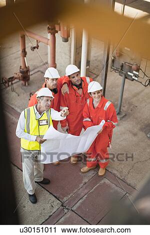 Stock Image - Workers with blueprints at oil refinery. Fotosearch