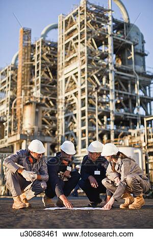 Stock Image - Workers with blueprints at oil refinery. Fotosearch