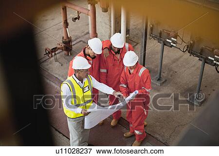 Stock Photo - Workers with blueprints at oil refinery. Fotosearch