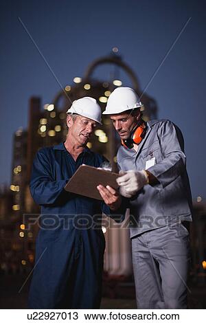 Stock Image - Workers with clipboard at oil refinery. Fotosearch