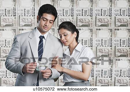 Stock Image - Business couple in front of a background of Indian currency notes. Fotosearch
